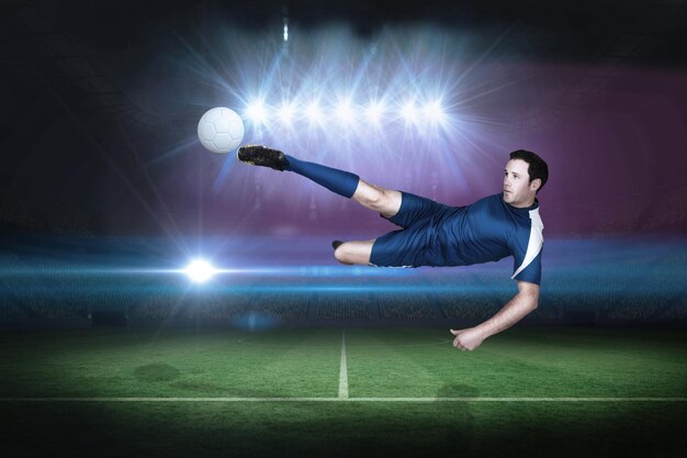 Foto jogador de futebol em azul chutando em um campo de futebol sob holofotes