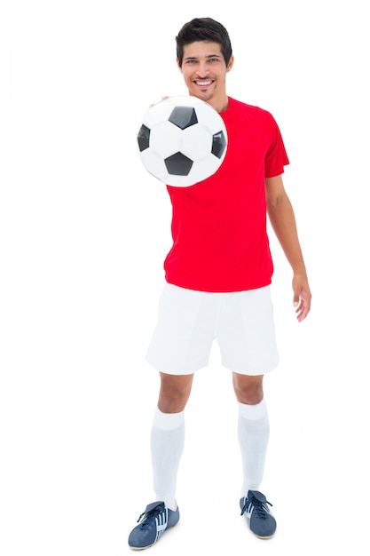 Jogador de futebol em vermelho mostrando bola