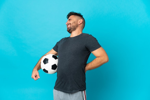 Jogador de futebol isolado em fundo azul com dor nas costas por ter feito esforço