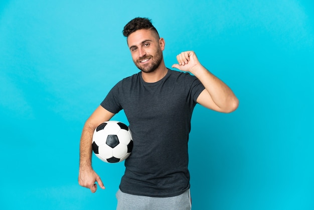 Jogador de futebol isolado em um fundo azul orgulhoso e satisfeito