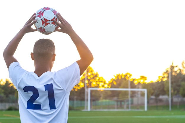 Jogador de futebol levantando a bola jogando Vista traseira do jogador de futebol jogando a bola com as mãos no campo de jogo Jogador de futebol fazendo jogando