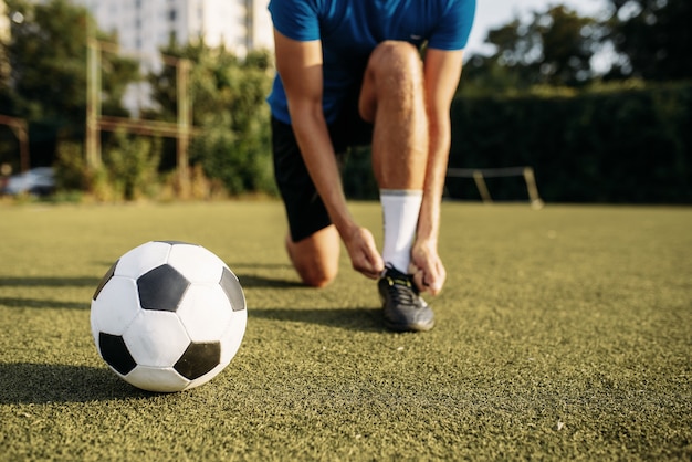 Jogador de futebol masculino amarra o cadarço nas botas, vista superior. Jogador de futebol no estádio ao ar livre, treino antes do jogo, treino de futebol