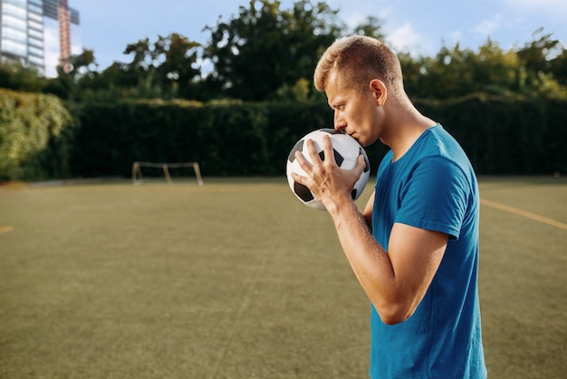 Jogador de futebol masculino com bola nas mãos no campo. Jogador de futebol no estádio ao ar livre, treino antes do jogo, treino de futebol