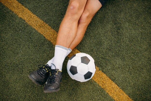 Jogador de futebol masculino com bola sentado na grama do campo. jogador de futebol no estádio ao ar livre, treino antes do jogo, treino de futebol