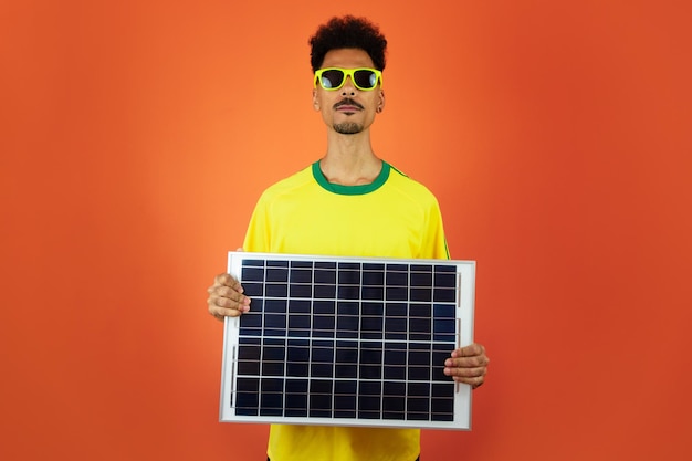 Jogador de futebol negro celebrando segurando painel solar fotovoltaico isolado em fundo laranja