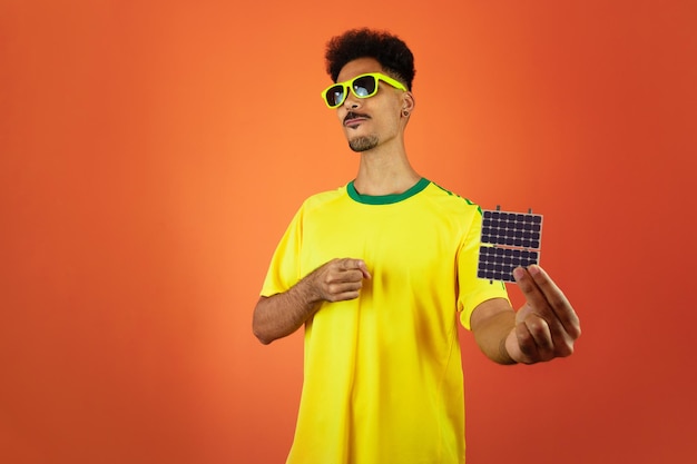 Jogador de futebol negro celebrando segurando painel solar fotovoltaico isolado em fundo laranja