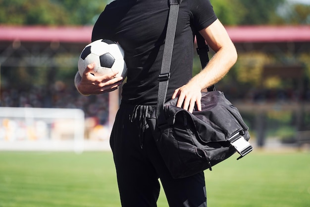Foto jogador de futebol no campo jovem esportivo de camisa preta e calças ao ar livre durante o dia