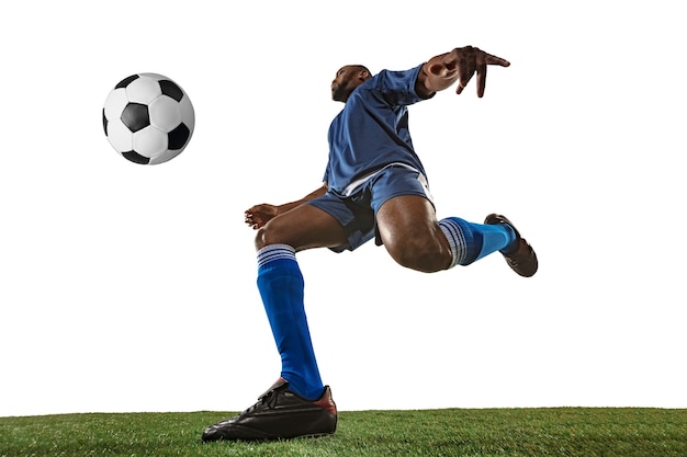 Foto jogador de futebol ou futebol em fundo branco com grama. jovem modelo desportivo masculino treinando, praticando. atacando, pegando. conceito de esporte, competição, vitória, movimento, superação. ângulo amplo.