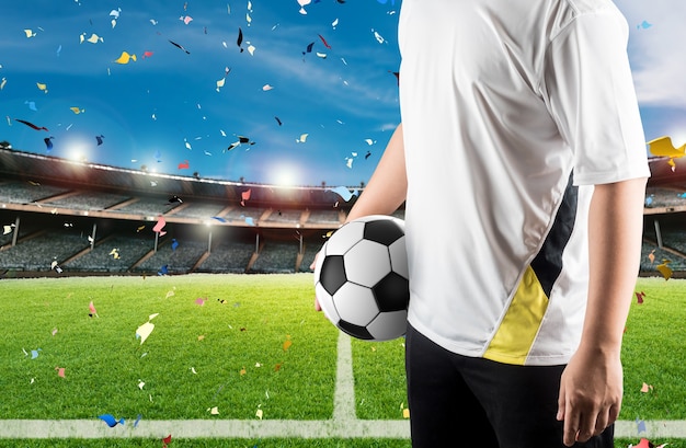 Jogador de futebol segurando uma bola com o fundo do estádio