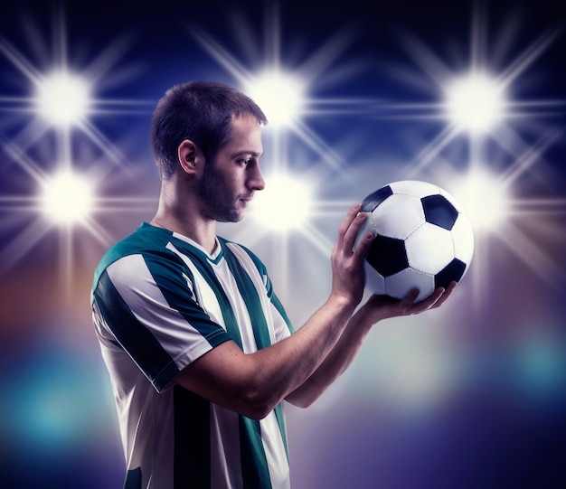 Jogador de futebol segurando uma bola sobre a superfície preta