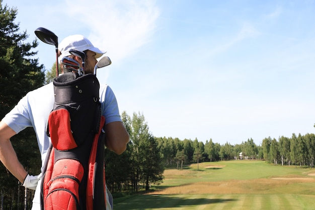 Foto jogador de golfe caminhando e carregando bolsa no curso durante o jogo de golfe de verão.