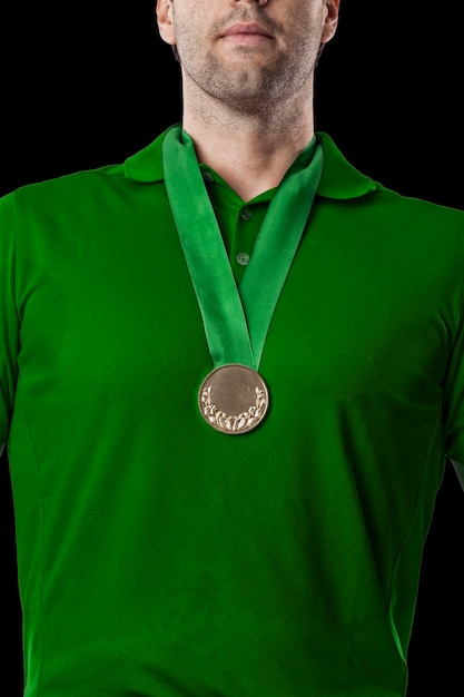 Jogador de golfe com camisa verde comemorando com medalha de ouro, sobre fundo preto.