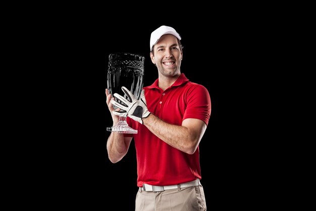 Jogador de golfe com uma camisa vermelha comemorando com um troféu de vidro nas mãos, sobre um fundo preto.