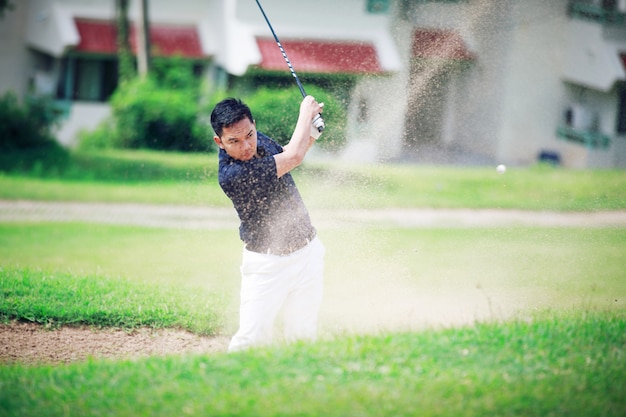 jogador de golfe do sexo masculino rebatendo de um trapgolfer de areia arremessando bola do bunker de areia em um campo de golfe em um dia ensolarado