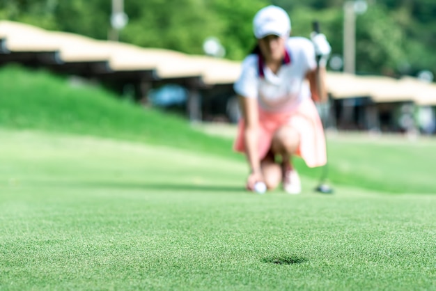 Jogador de golfe feminino profissional jovem agachado e estudar o verde antes de colocar o tiro