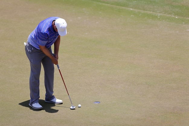 Jogador de golfe masculino vestindo camisa branca, colocando em dia ensolarado