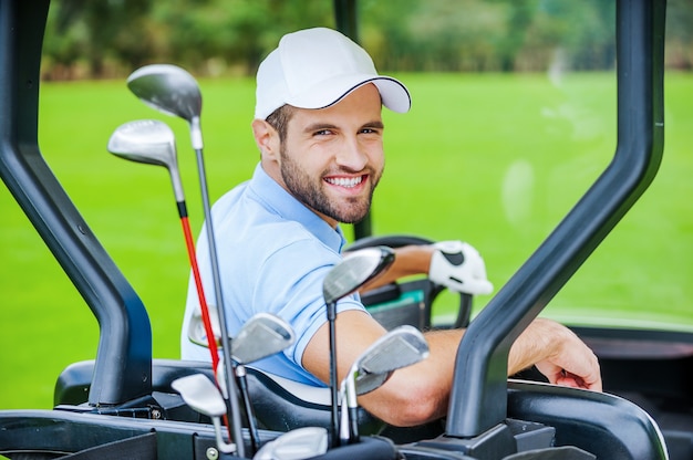 Jogador de golfe no carrinho de golfe. Retrovisor de um jovem jogador de golfe feliz dirigindo um carrinho de golfe e olhando por cima do ombro