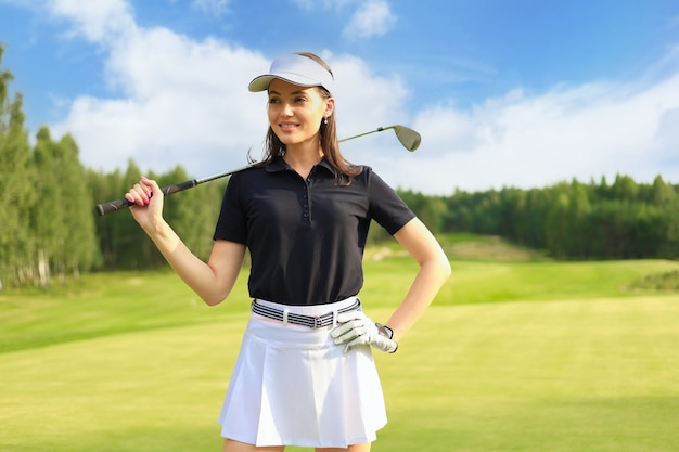 Jogador de golfe profissional feminino segurando o clube de golfe no campo e desviar o olhar. Jovem mulher de pé no campo de golfe em um dia ensolarado.