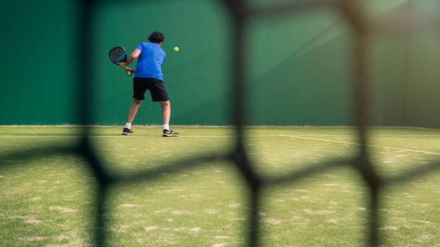 Jogador de padel com raquete preta jogando uma partida ao ar livre atrás da quadra da rede