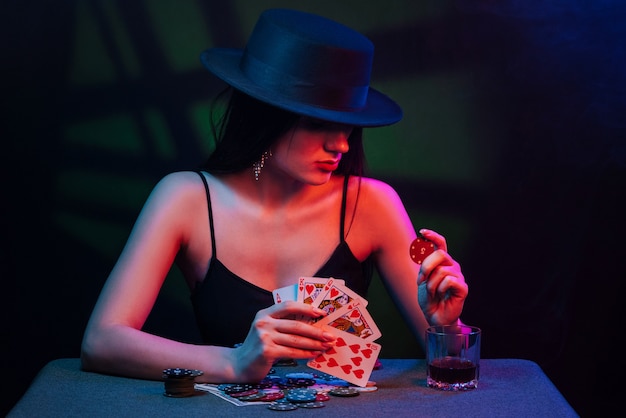 Jogador de pôquer em uma mesa de cassino com cartas e fichas. A mulher do chapéu está jogando
