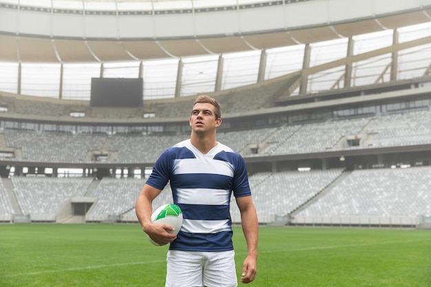 Jogador de rugby caucasiano de pé com uma bola de rugby no estádio
