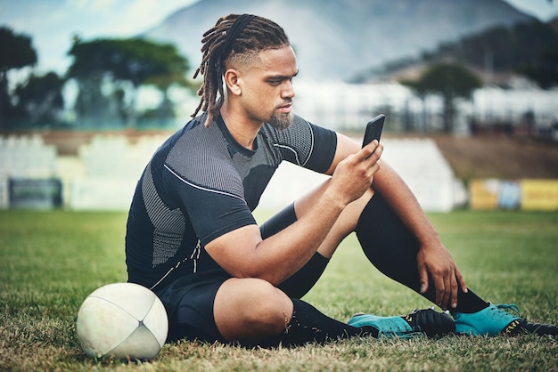 Jogador de rugby e bola no campo para comunicação móvel e streaming de vídeo do jogo com internet Black man smartphone e mídias sociais na grama para site de aplicativo esportivo e podcast motivacional