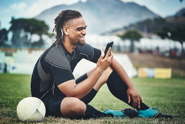 jogador de rugby e feliz no campo para comunicação móvel e streaming jogo on-line com internet homem africano telefone e mídias sociais na grama para esportes app chamada de vídeo e podcast motivacional