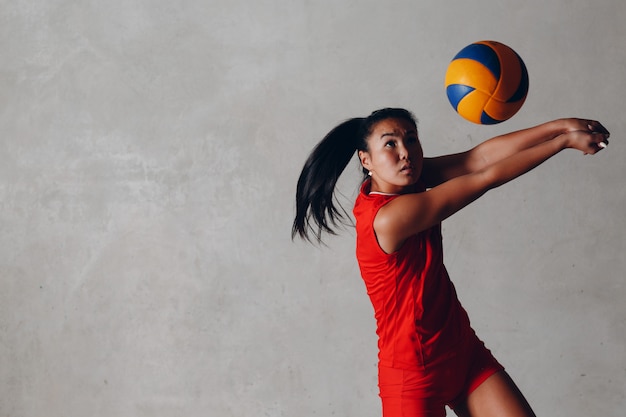 Foto jogador de voleibol jovem mulher asiática em uniforme vermelho leva bola