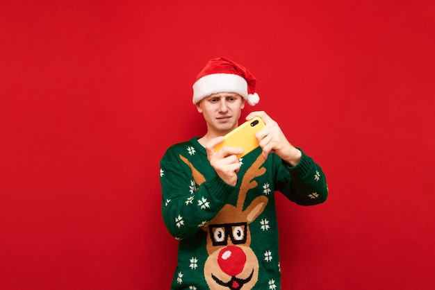 jogador em roupas de natal jogando jogos para celular em smartphone isolado em fundo vermelho