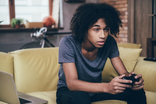 Jogador exausto. Jovem africano segurando um joystick e parecendo exausto enquanto está sentado no sofá em casa