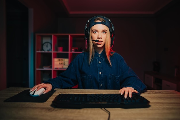 Jogador feminino surpreso em um boné e fone de ouvido joga videogame em casa no computador