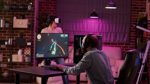 Jogador jogando atirador espacial multiplayer enquanto a garota do jogo está lutando no jogo de realidade virtual em casa. homem transmitindo jogo de ação online no pc enquanto a garota de jogos usa óculos de realidade virtual para simulação.