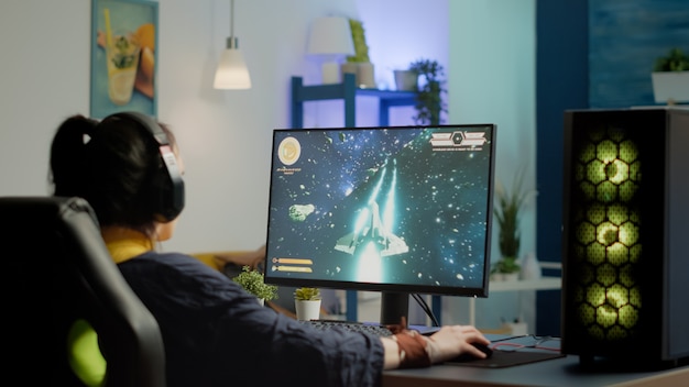 Jogador mulher concentrada colocando fone de ouvido começando a jogar videogame de atirador espacial em competição virtual em um poderoso computador pessoal. Esport cyber se apresentando durante o torneio de jogos esport