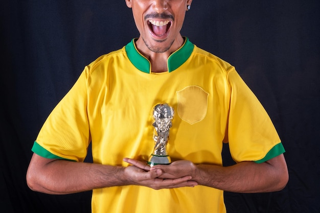 Foto jogador negro de futebol brasileiro segurando o troféu do vencedor e comemorando