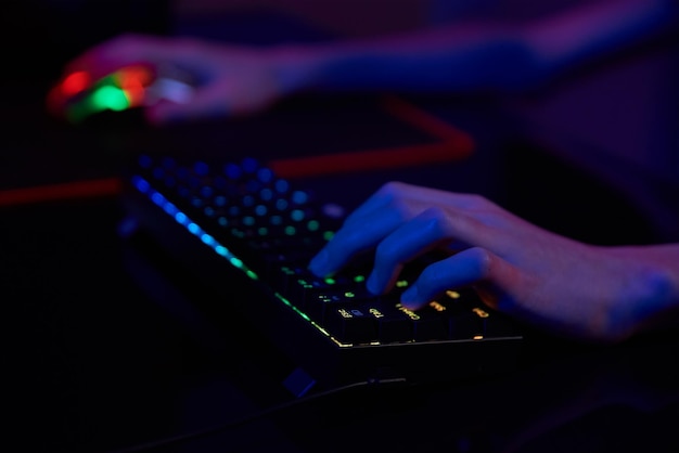 Jogador profissional joga videogame de computador em sala escura, use teclado mecânico rgb colorido neon para jogos cibernéticos