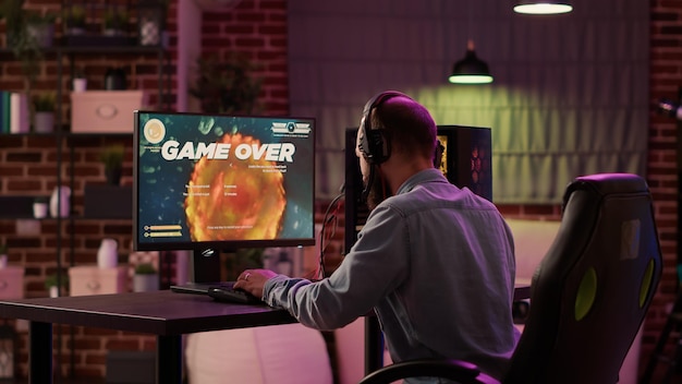Jogador se sentindo decepcionado depois de perder o nível difícil no atirador espacial online no PC para jogos na sala de estar em casa. Homem jogando jogo multiplayer de internet triste e entediado depois de falhar no torneio.