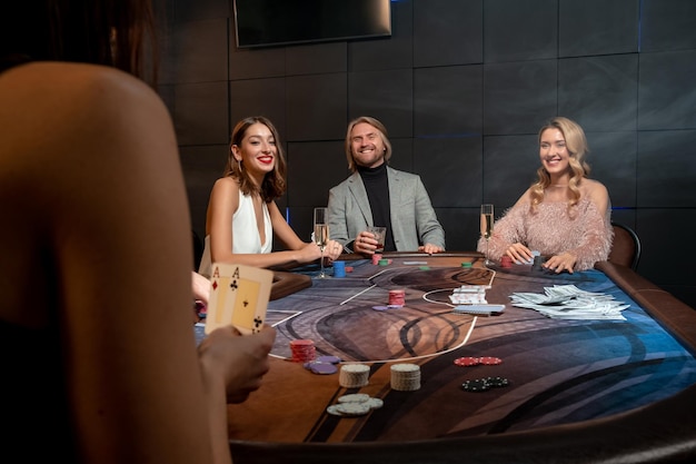 Jogadores de pôquer sorridentes sentados na mesa de jogos com cartas e bebidas alcoólicas