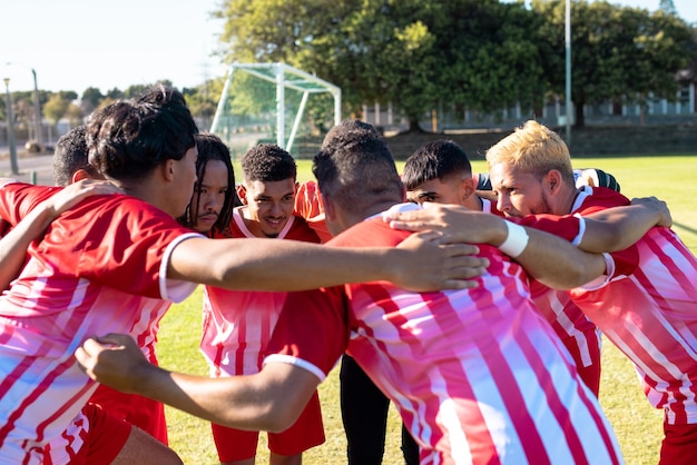 Jogadores multirraciais da equipe masculina em uniformes vermelhos, amontoados e discutindo no playground durante a partida