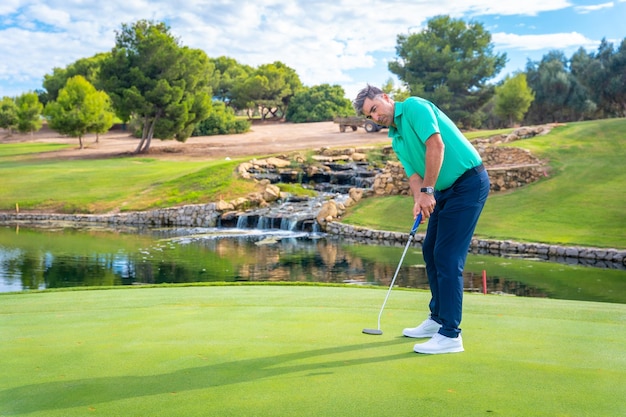 Jogando golfe no clube de golfe por um lago no verde batendo na bola com o taco