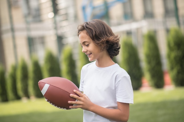 Jogando. menino de cabelos escuros em uma camiseta branca brincando com uma bola