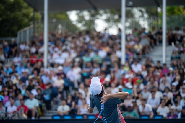 jogando tênis em uma quadra de tênis azul servindo em uma quadra de tênis com uma multidão de fãs assistindo no Aberto da Austrália