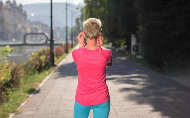 Joggende Frau, die Musik einstellt und die Strecke auf dem Smartphone läuft, Kopfhörer vor dem morgendlichen Lauf aufsetzt