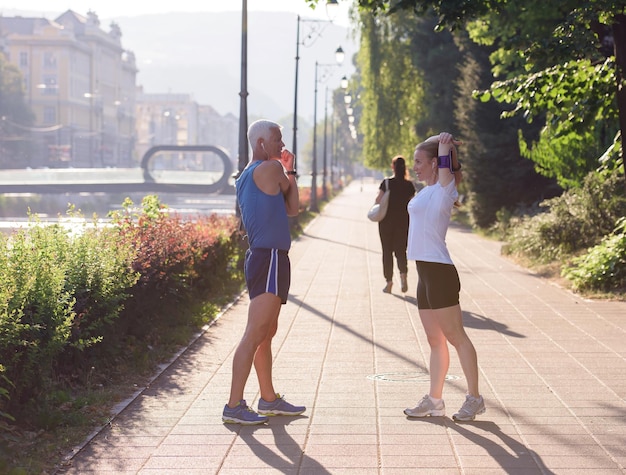 Joggendes Paar, das sich vor dem morgendlichen Lauftraining in der Stadt mit Sonnenaufgang im Hintergrund aufwärmt und dehnt