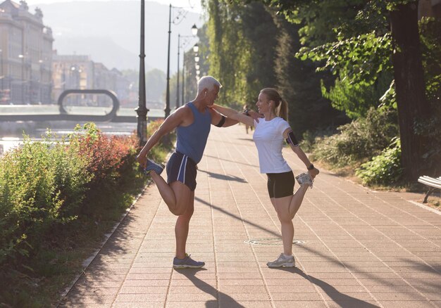 Joggendes Paar, das sich vor dem morgendlichen Lauftraining in der Stadt mit Sonnenaufgang im Hintergrund aufwärmt und dehnt