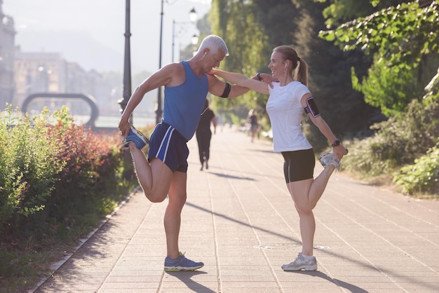 Joggendes Paar, das sich vor dem morgendlichen Lauftraining in der Stadt mit Sonnenaufgang im Hintergrund aufwärmt und dehnt