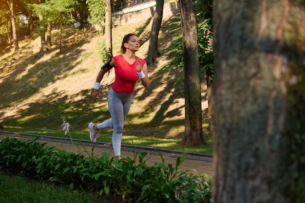 Jogger deportivo de mujer caucásica de mediana edad activa de longitud completa haciendo ejercicio al aire libre corriendo en una cinta de correr en un parque de la ciudad en un día soleado y cálido de verano Concepto de entrenamiento funcional de fitness deportivo