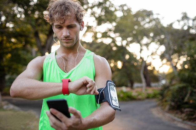 Jogger escuchando música en el teléfono móvil y revisando su reloj inteligente