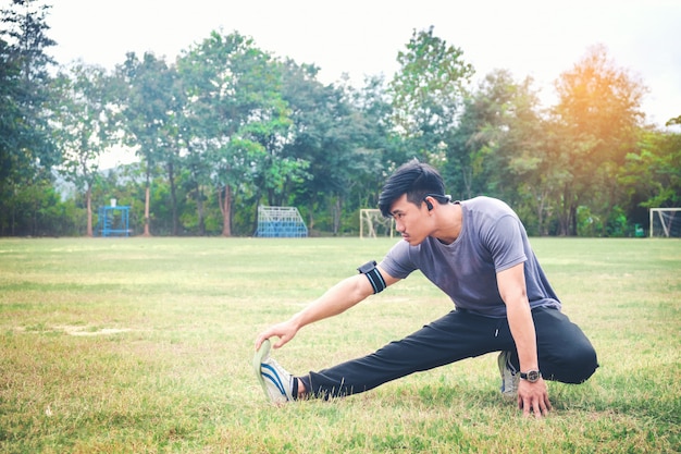 Jogger guapo joven usando rastreador de fitness estirando una pierna por el lago en el parque