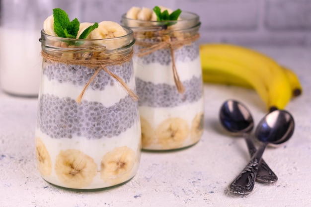 Joghurt mit Banane und Müsli in Gläsern auf weißem Hintergrund.