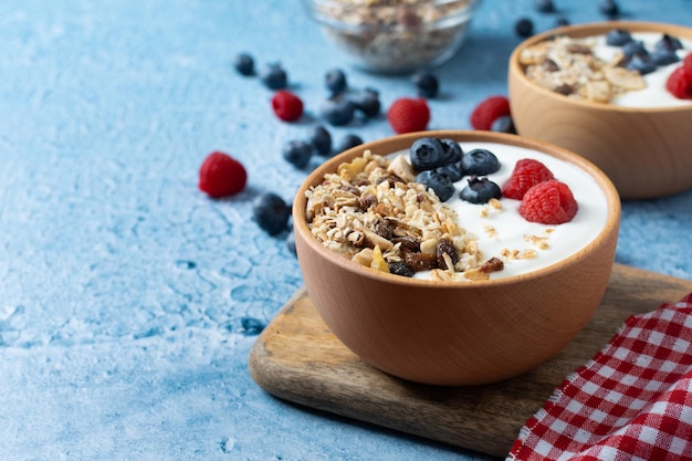 Joghurt mit Beeren und Müsli zum Frühstück in Schüssel auf blauem Hintergrund